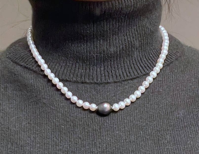 A single Tahitian pearl in the center of a white pearl strand